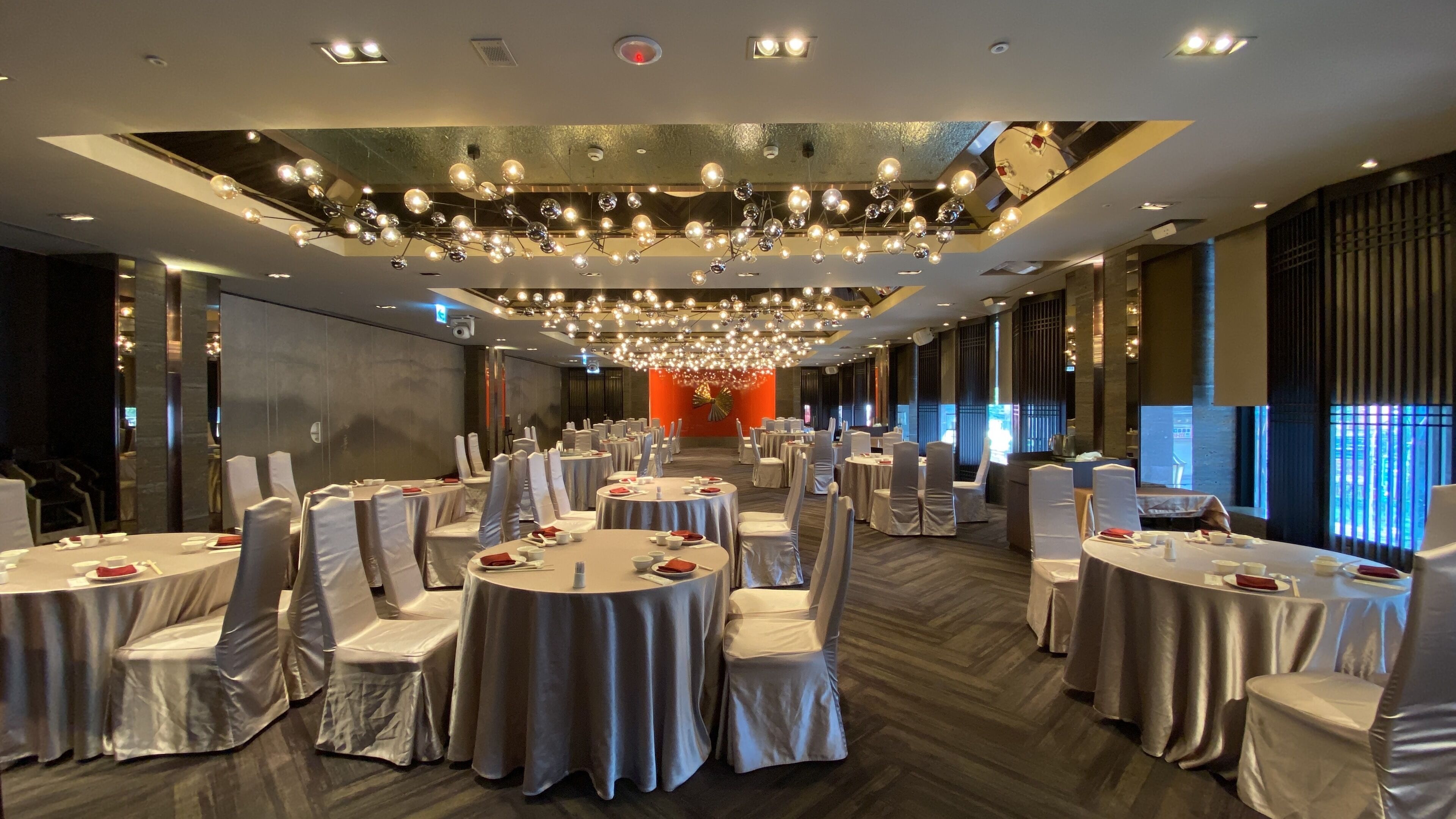 A banquet hall with round tables, white chairs, and a chandelier.