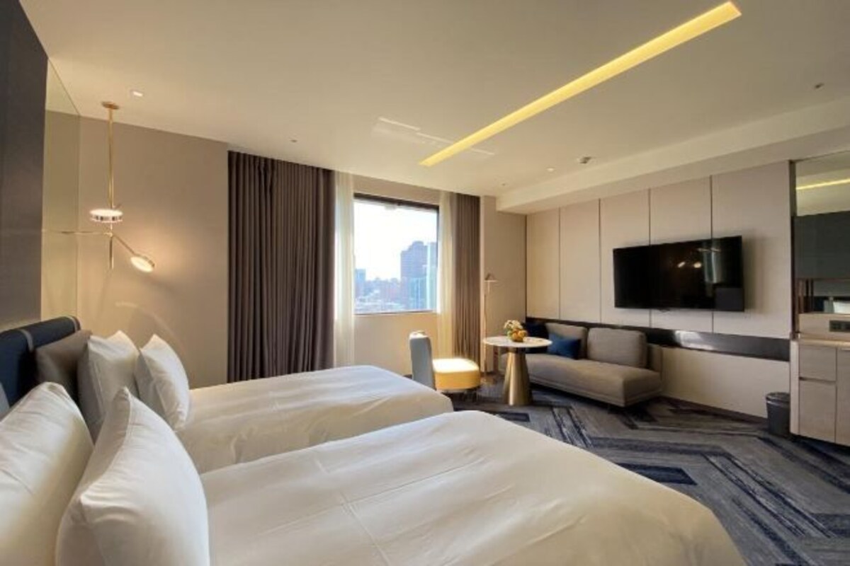 Une chambre d’hôtel avec deux lits, un canapé, une télévision et une vue sur la ville.