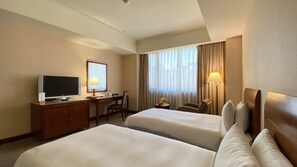 Habitació d'hotel amb dos llits, una escriptori amb televisió, una làmpada i una finestra amb cortines.