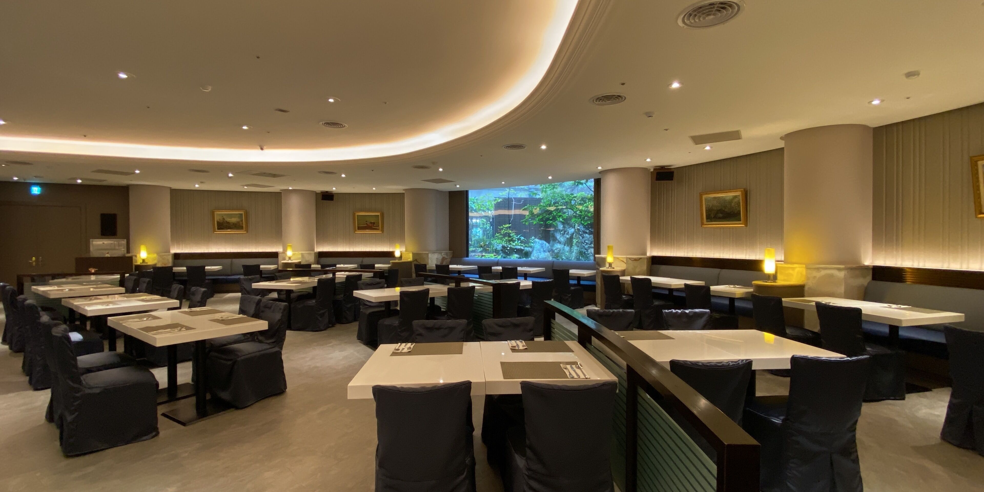 A modern dining area with multiple tables and chairs, recessed lighting, and framed artwork on the walls.