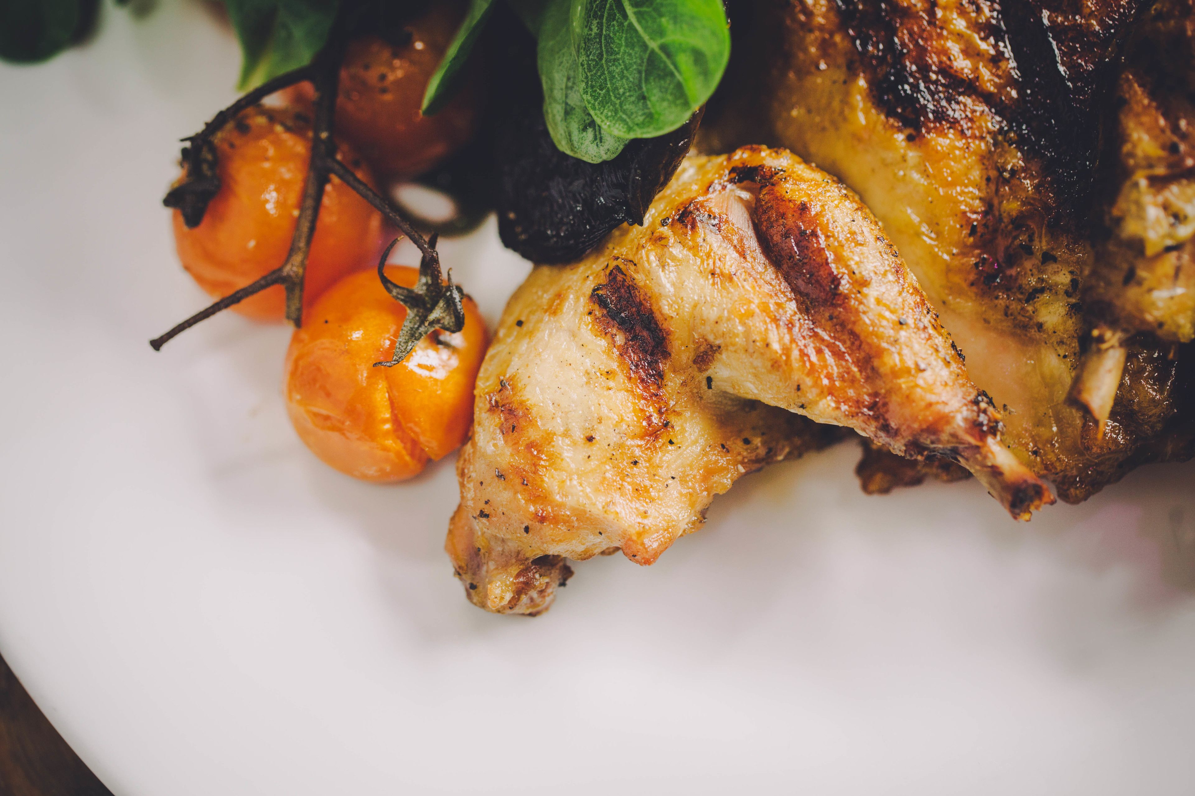 Une vue rapprochée d’un poulet rôti, garni d’herbes aromatiques et de tomates cerises, présenté sur une assiette.