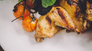 Une vue rapprochée d’un poulet rôti, garni d’herbes aromatiques et de tomates cerises, présenté sur une assiette.