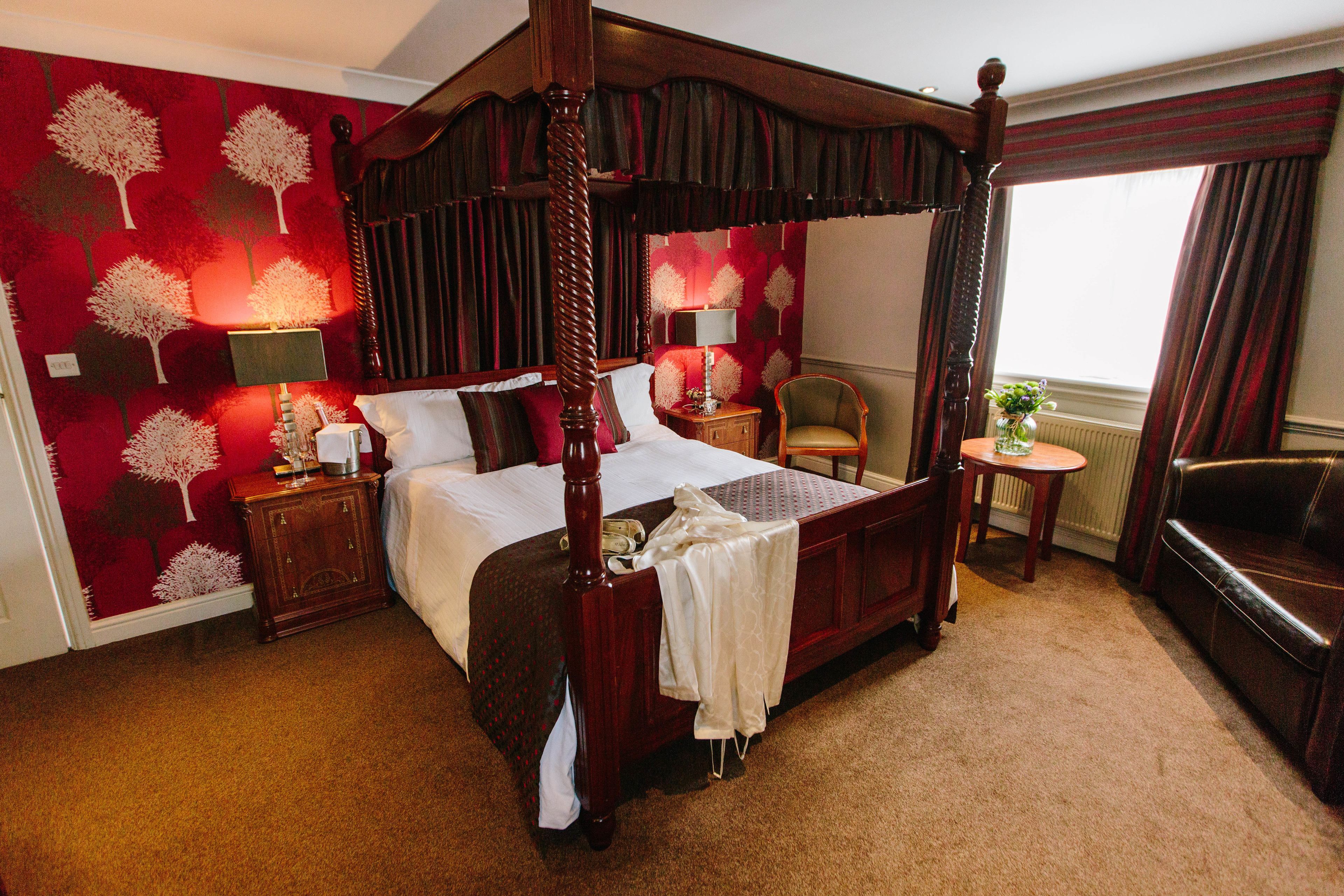 A four-poster bed with a canopy, a nightstand, a chair, and a small table with a vase of flowers.