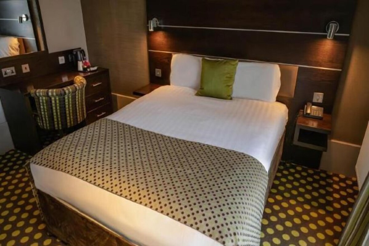 Una habitación de hotel con una cama grande, una mesita de noche, un aparador y una alfombra estampada.