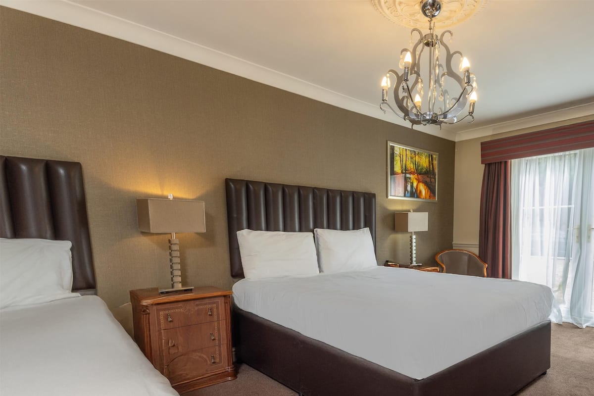 Una habitación de hotel con una cama grande, dos mesitas de noche, un candelabro y un cuadro en la pared.