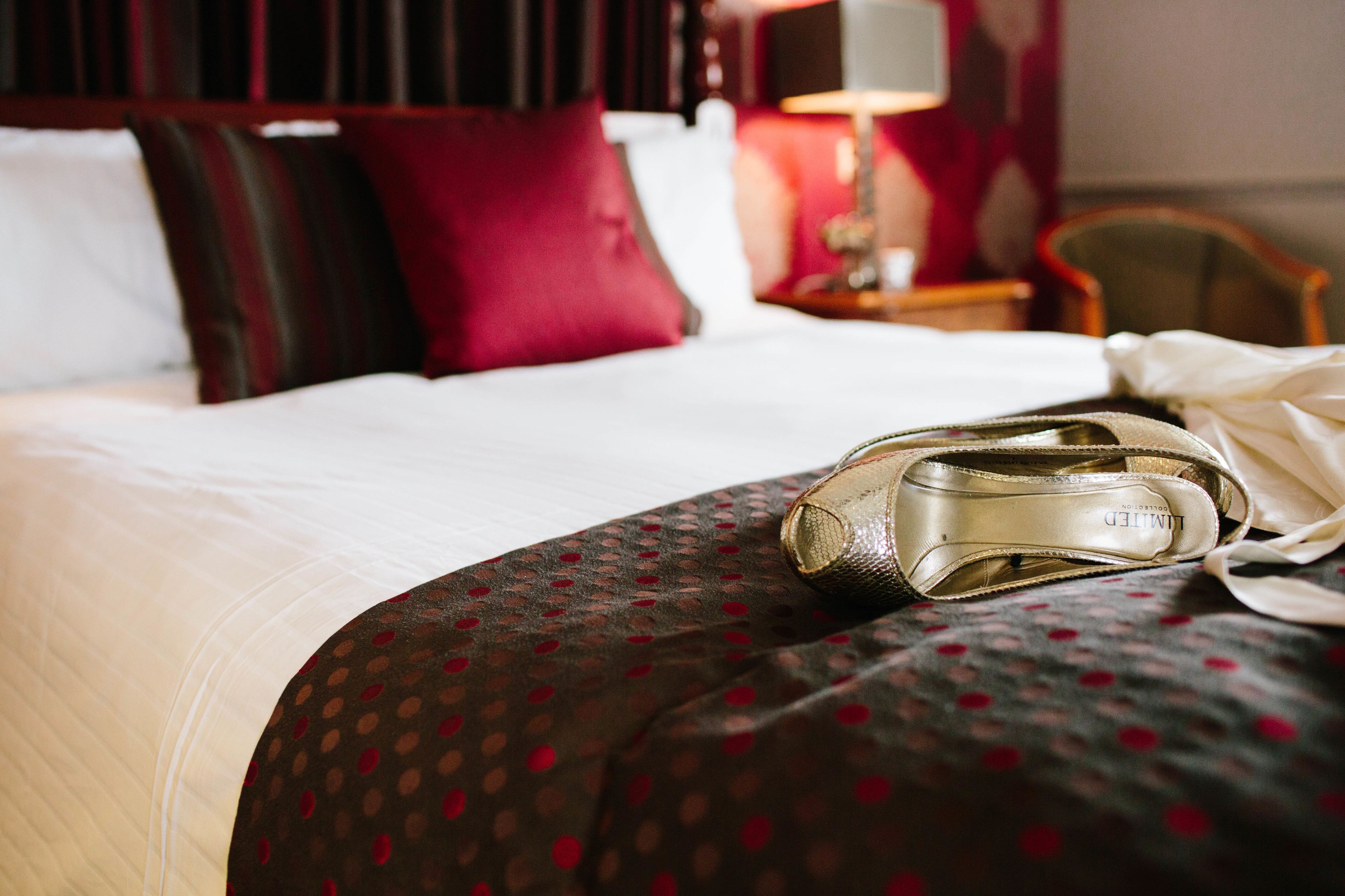 Ein Hotelzimmer mit einem Bett, einem Schuhpaar auf dem Bett, einer Lampe und einem Sessel.