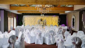 A banquet hall with round tables set for a wedding reception, featuring white tablecloths and chairs with bows.
