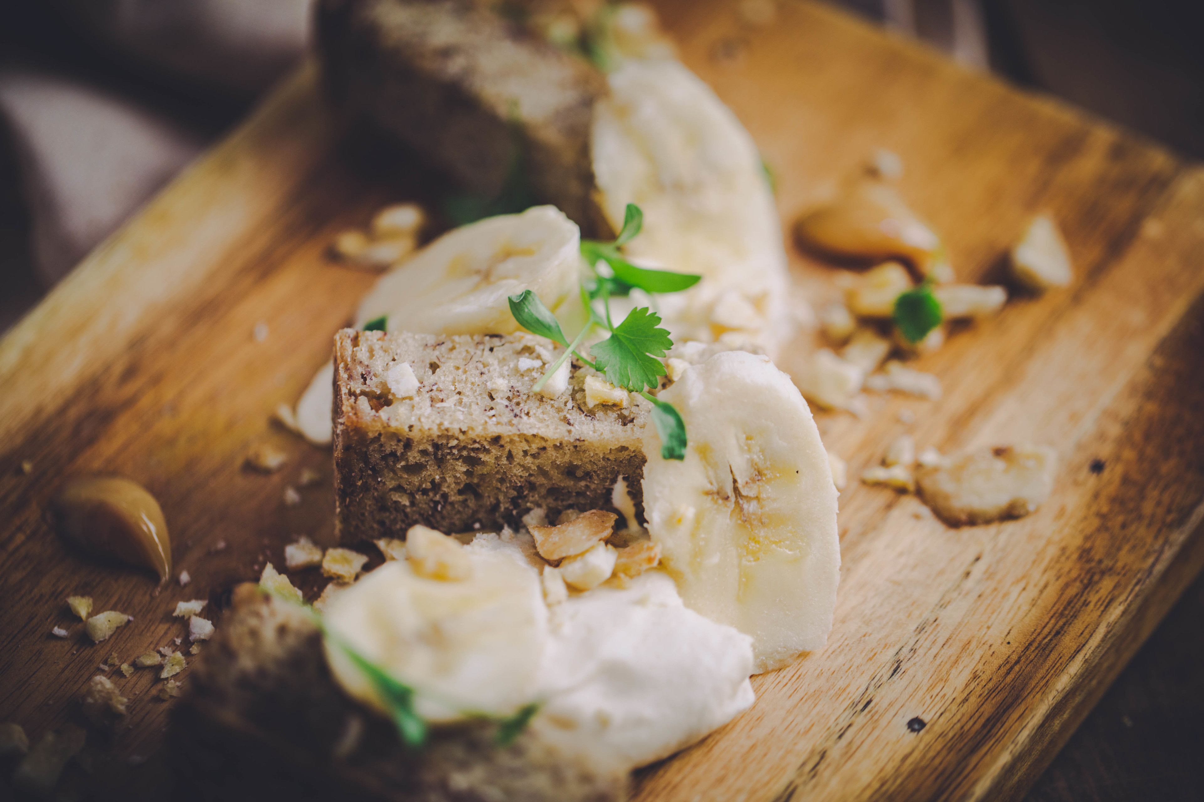 Ein Holzschnittbrett mit Brot, Bananenstücken und ein paar grünen Kräutern.
