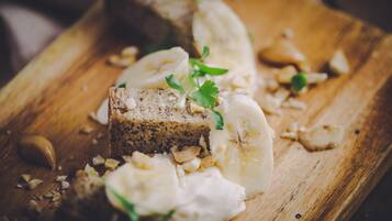 Ein Holzschnittbrett mit Brot, Bananenstücken und ein paar grünen Kräutern.