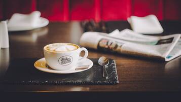 A cup of coffee on a saucer with a spoon beside it, a newspaper, and a napkin on a dark placemat.