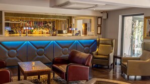Zona de bar con varias botellas de licores y una barra. Hay sofás de cuero y una mesa pequeña en la zona de estar.