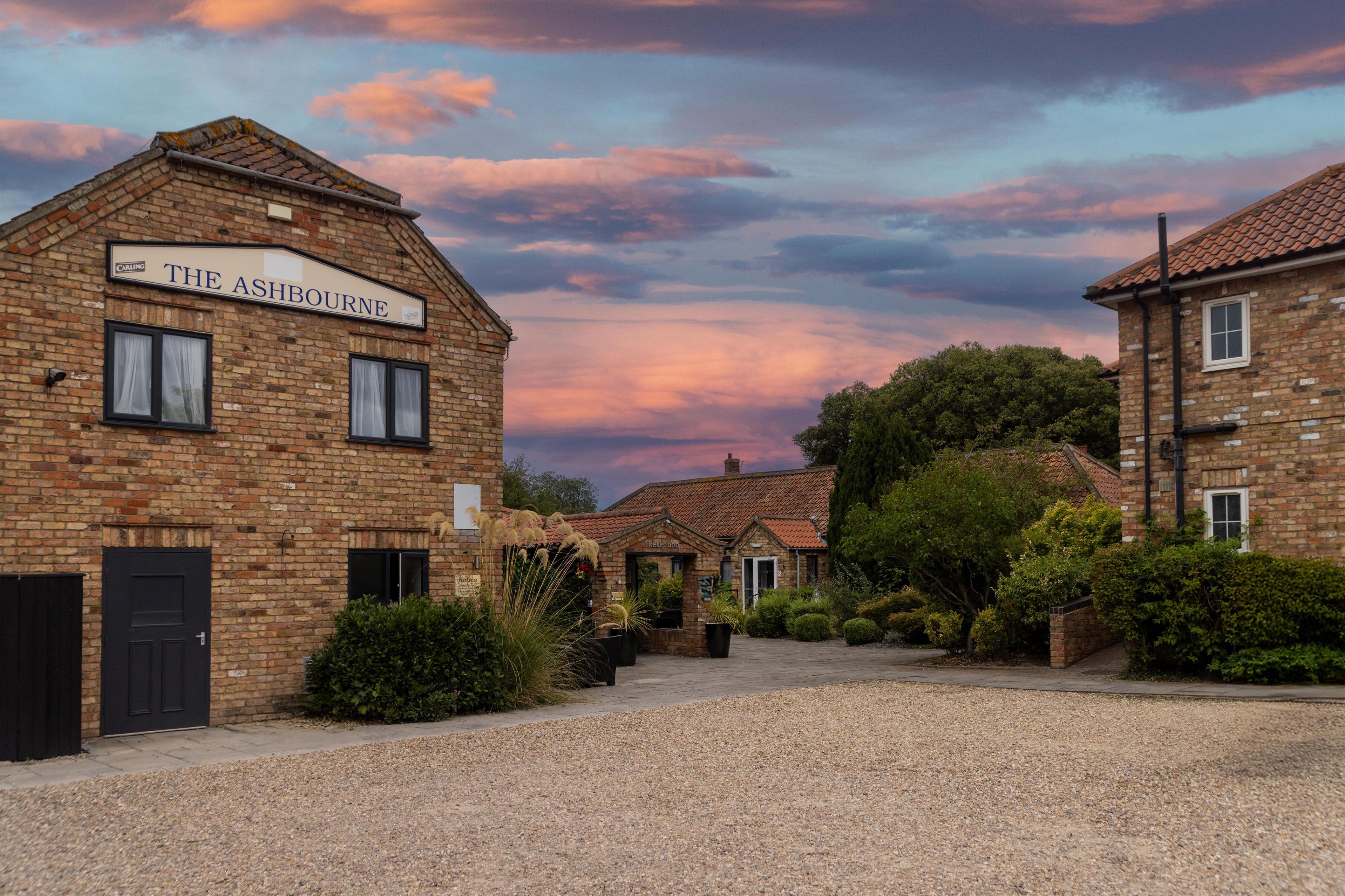A brick building labeled "The Ashbourne" with a gravel driveway and surrounding greenery.