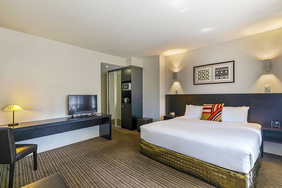 Une chambre d’hôtel comprenant un lit, un bureau avec une télévision, une lampe et une table de chevet.