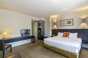 A hotel room with a bed, a desk with a TV, a lamp, and a nightstand.