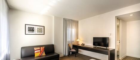 A hotel room with a bed, a black leather sofa, a desk with a TV, and a chair.
