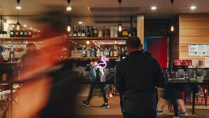 A bar area with shelves of bottles, hanging lights, and a neon sign. - Causeway 353 Hotel (Melbourne)