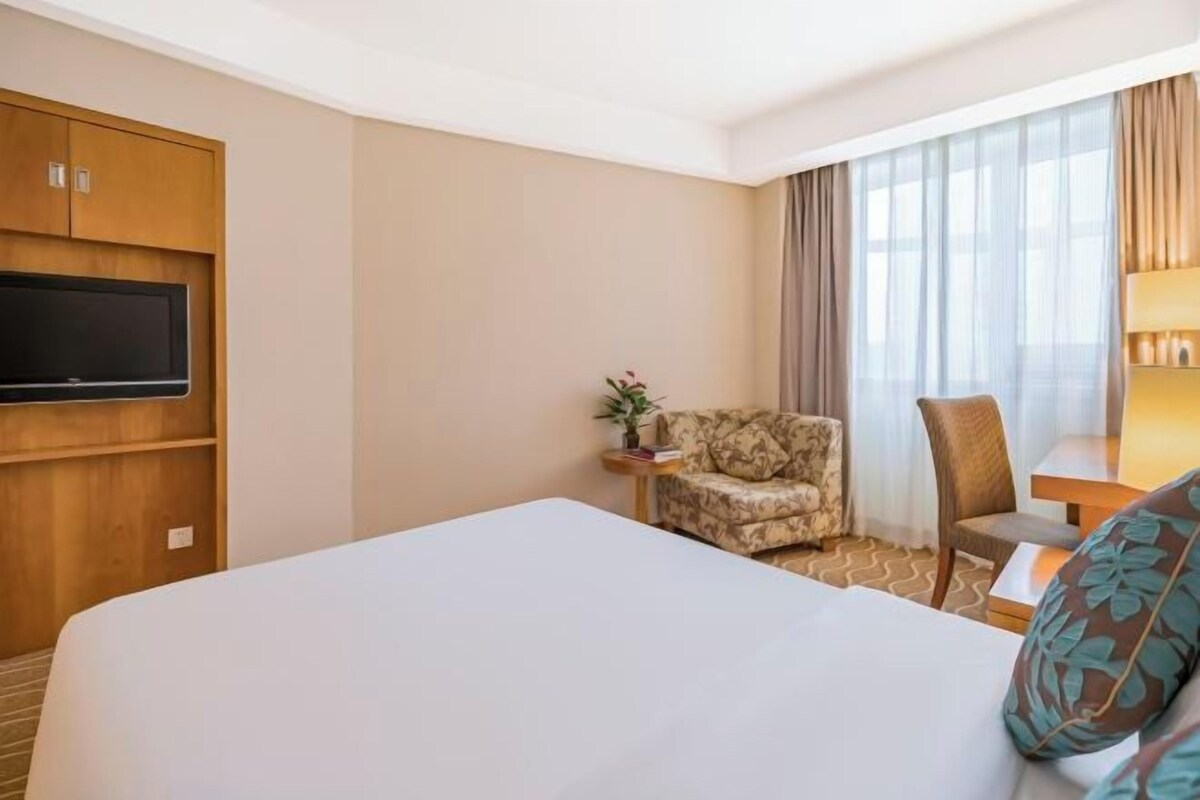 Habitació d'hotel amb un llit gran, televisió penjada a la paret, una taula petita amb una làmpada i dues cadires.