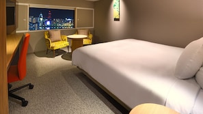 Une chambre d’hôtel avec un lit, un bureau, une chaise, une petite table et une vue sur le paysage urbain illuminé la nuit.