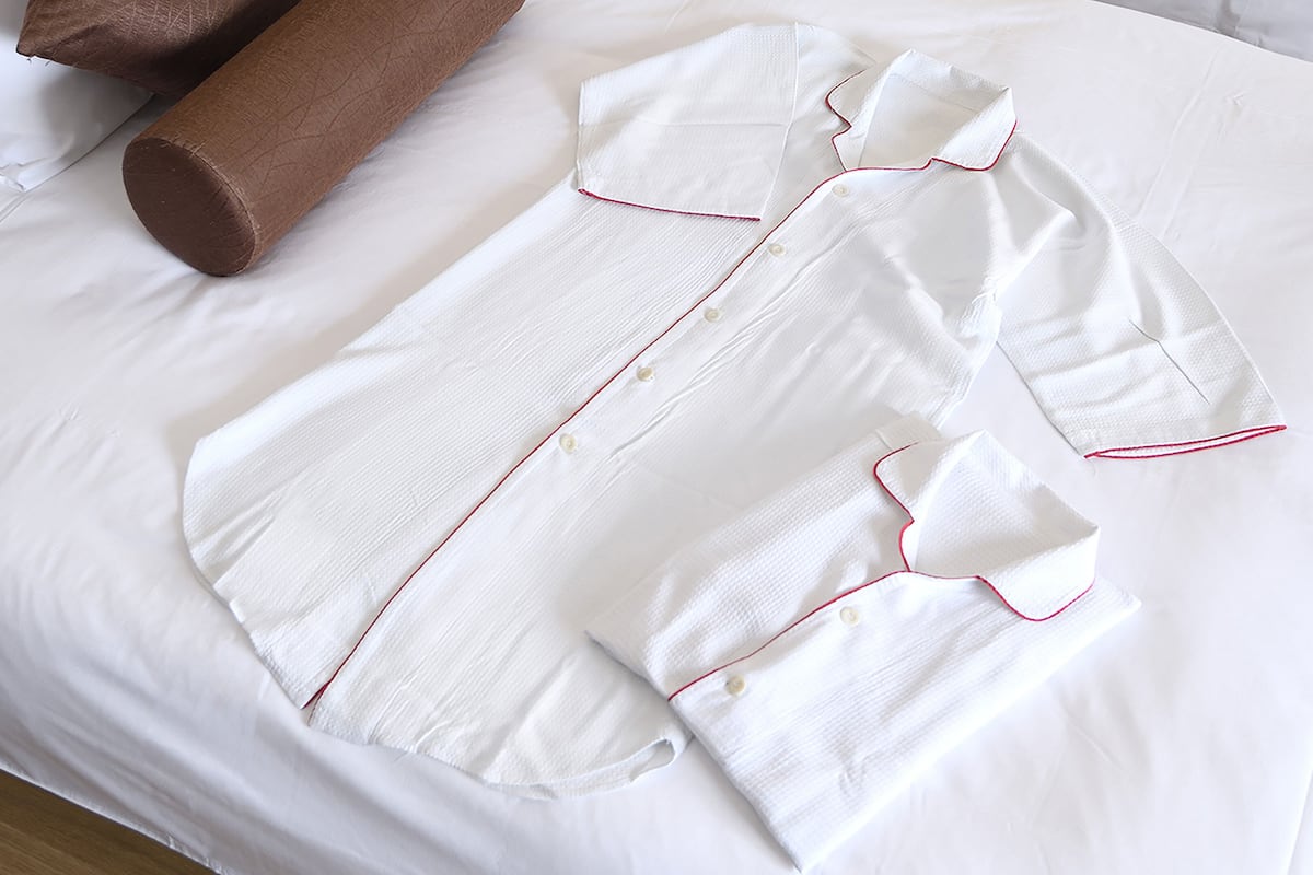 A neatly made bed with white bedding and a white shirt laid out on it.