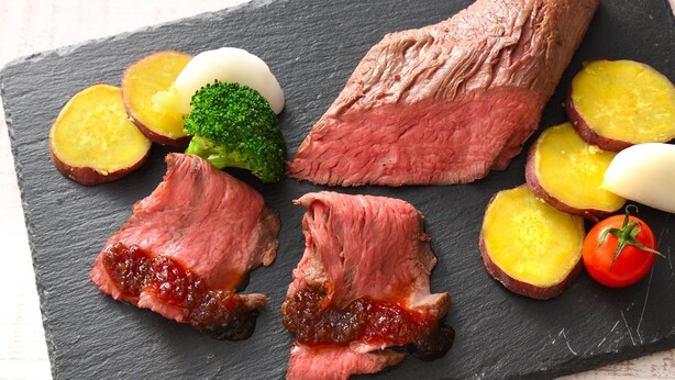 Un repas composé de tranches de viande, d’œufs durs, de pommes de terre, de brocolis et d’une tomate, le tout présenté sur une planche en ardoise.