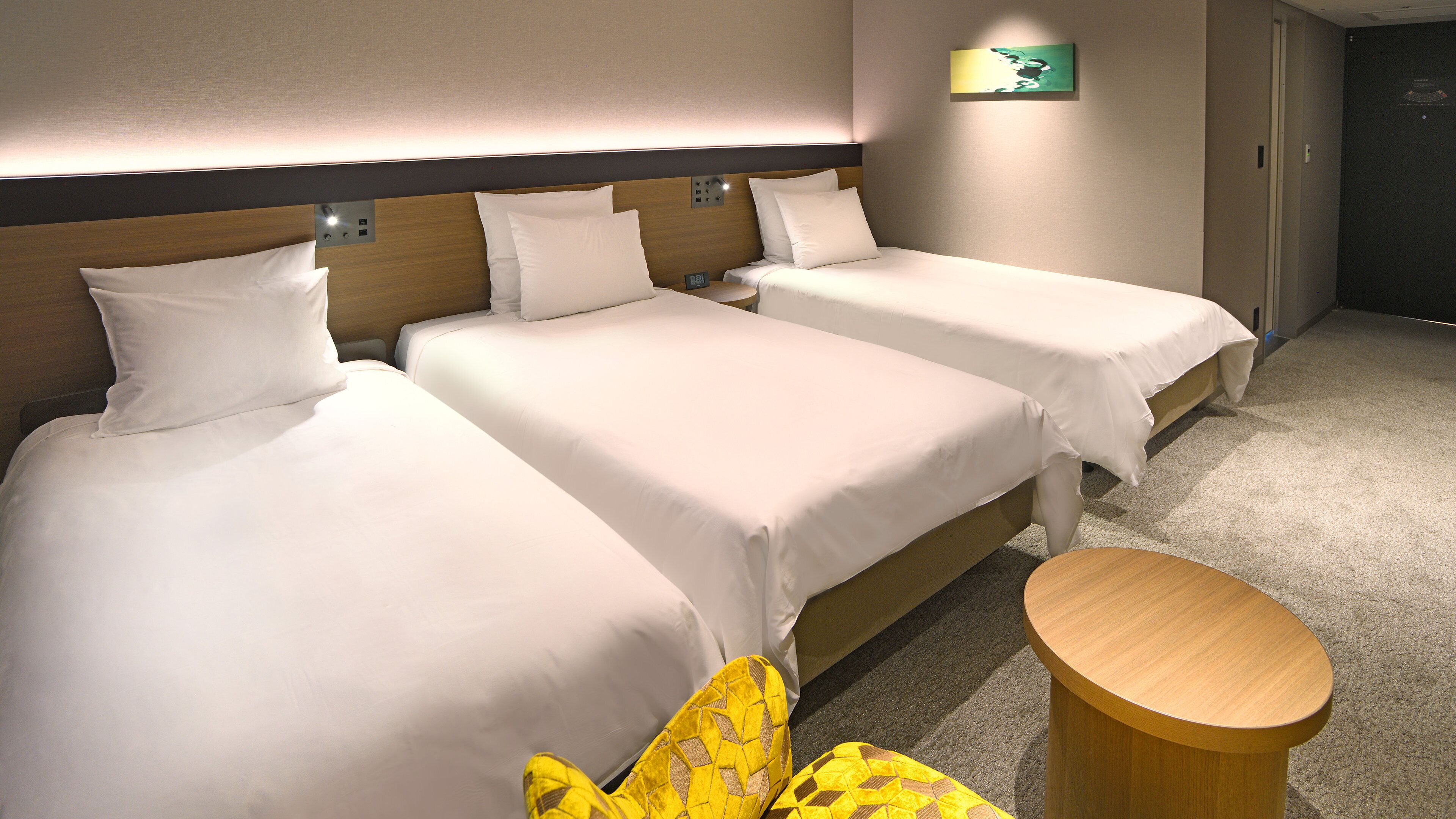 Quarto de hotel com três camas, uma pequena mesa de cabeceira de madeira e piso coberto por carpete.