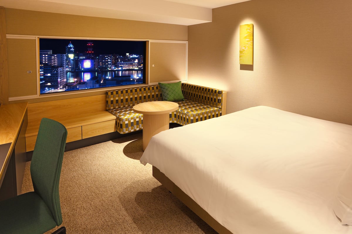 Habitación de hotel con cama, zona de estar y vista a la ciudad de noche, y una pequeña mesa redonda.
