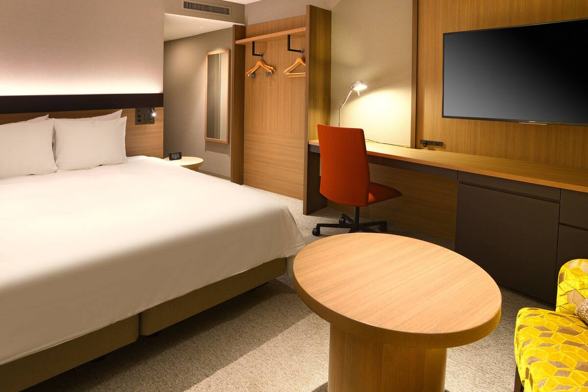 Ein Hotelzimmer mit einem großen Bett, einem Schreibtisch, einem Stuhl, einem Fernseher und einem Kleiderschrank.
