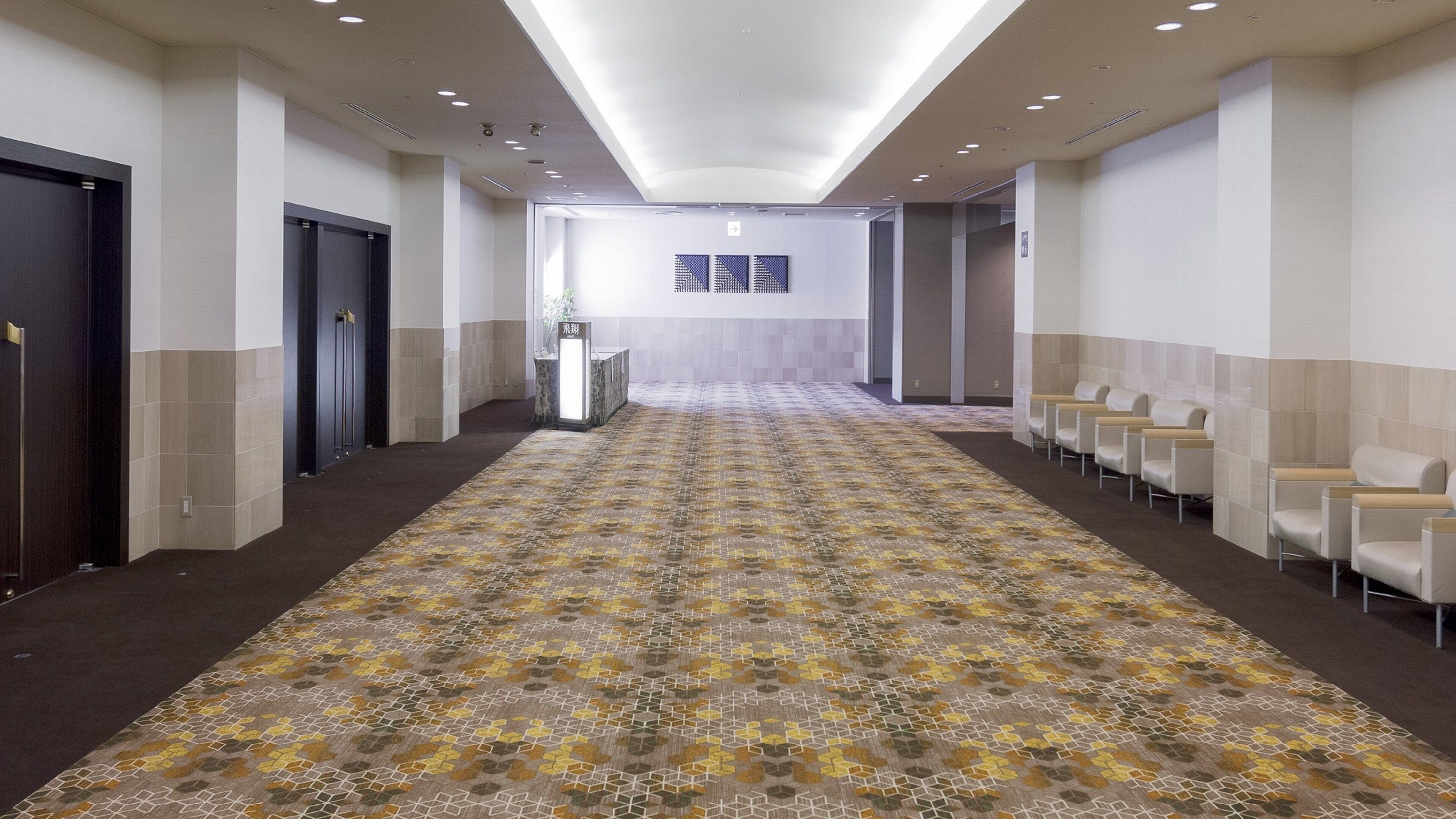 A hotel hallway with a patterned carpet, a reception desk, and seating area.