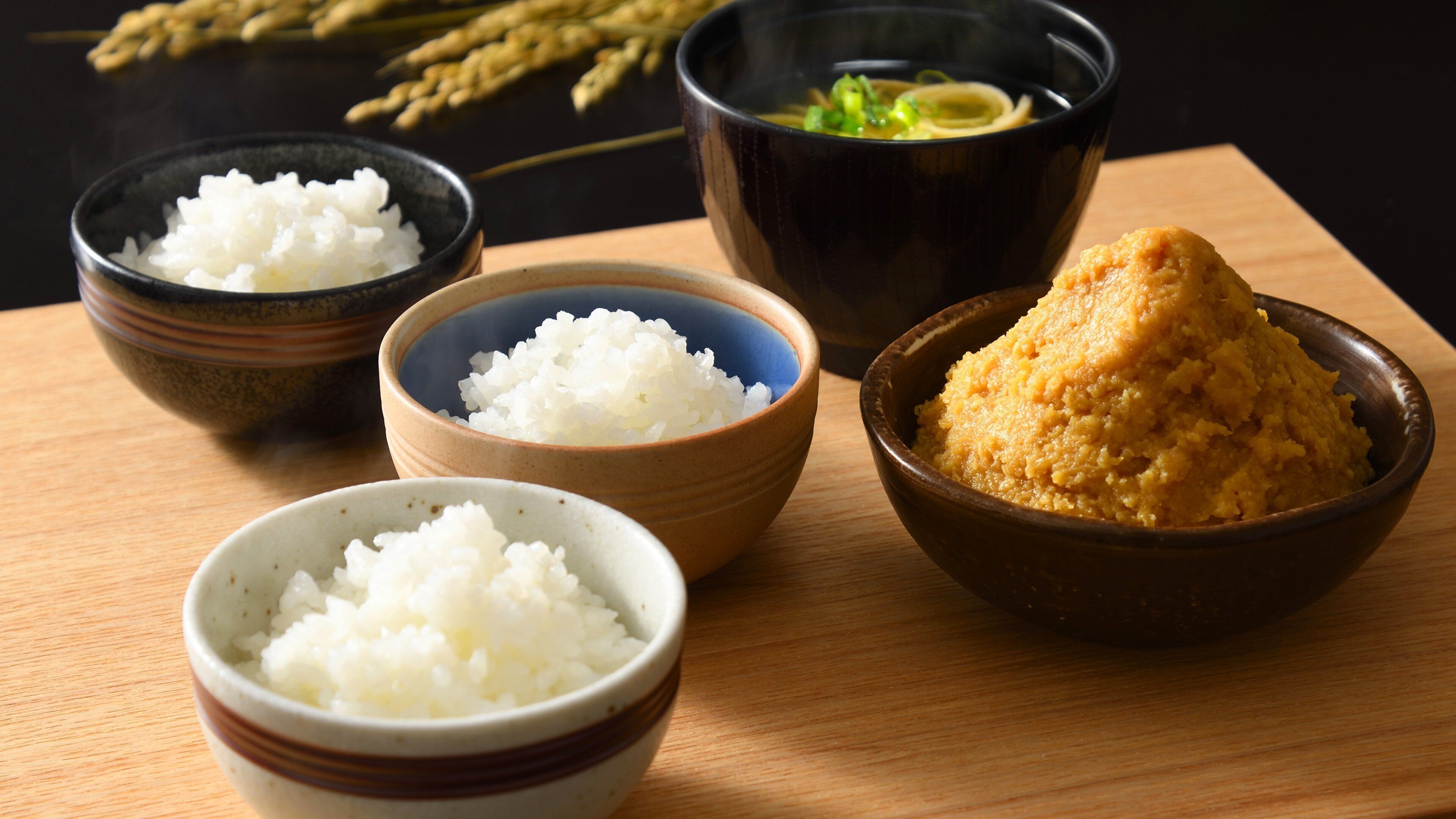 Four bowls of rice and a bowl of miso soup on a wooden table.