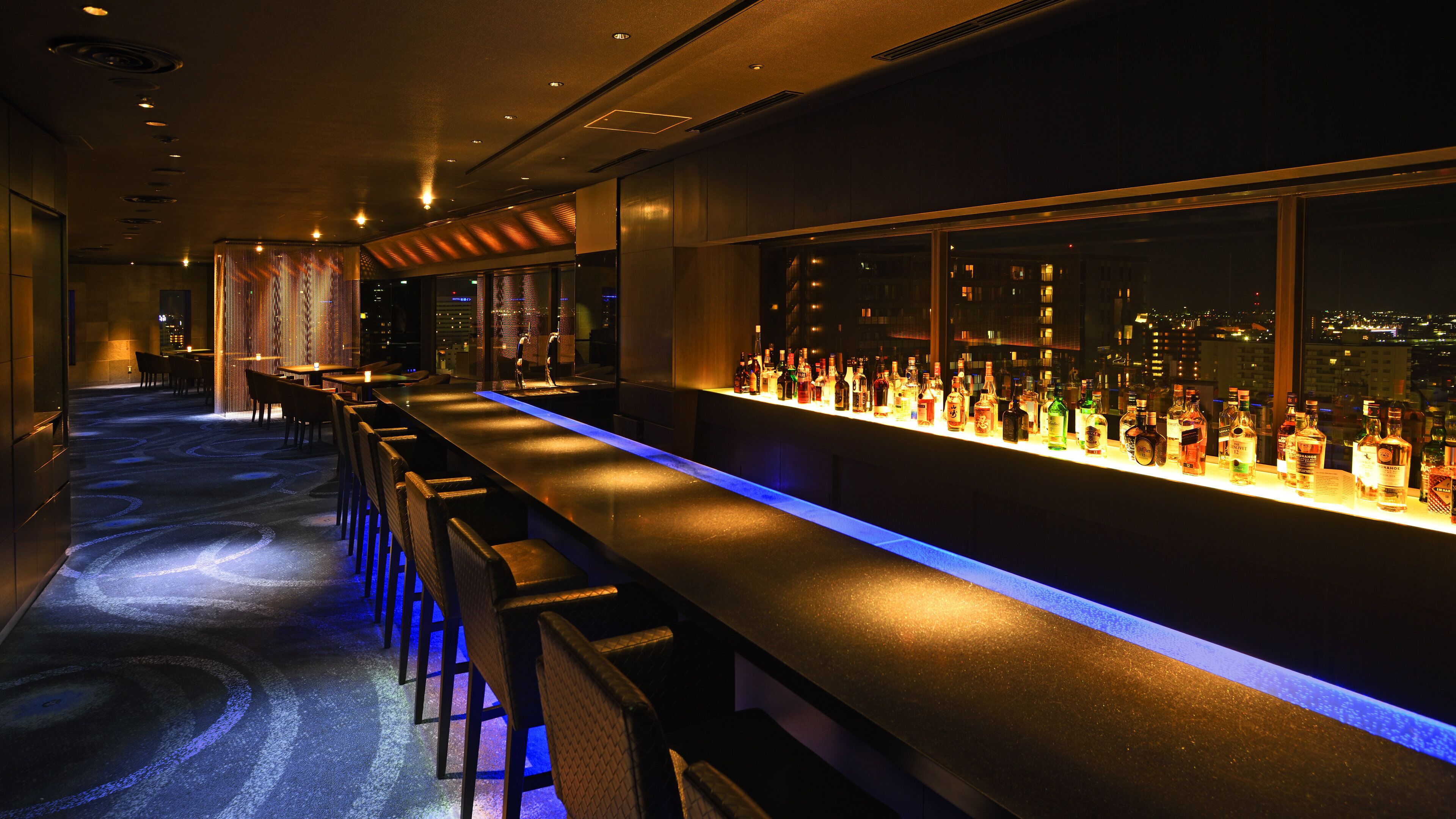A bar area with a long counter, bar stools, and a city view through the window.