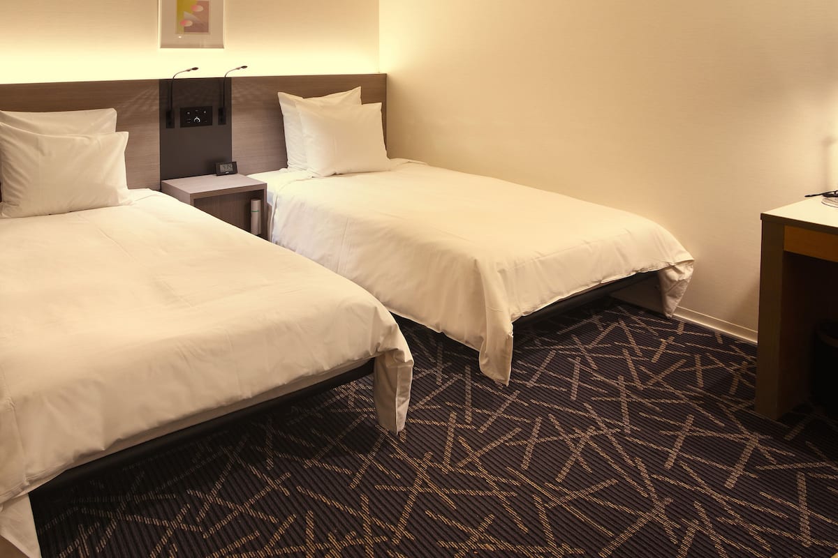 Una habitación de hotel con dos camas individuales, una mesita de noche, una lámpara y una alfombra estampada.