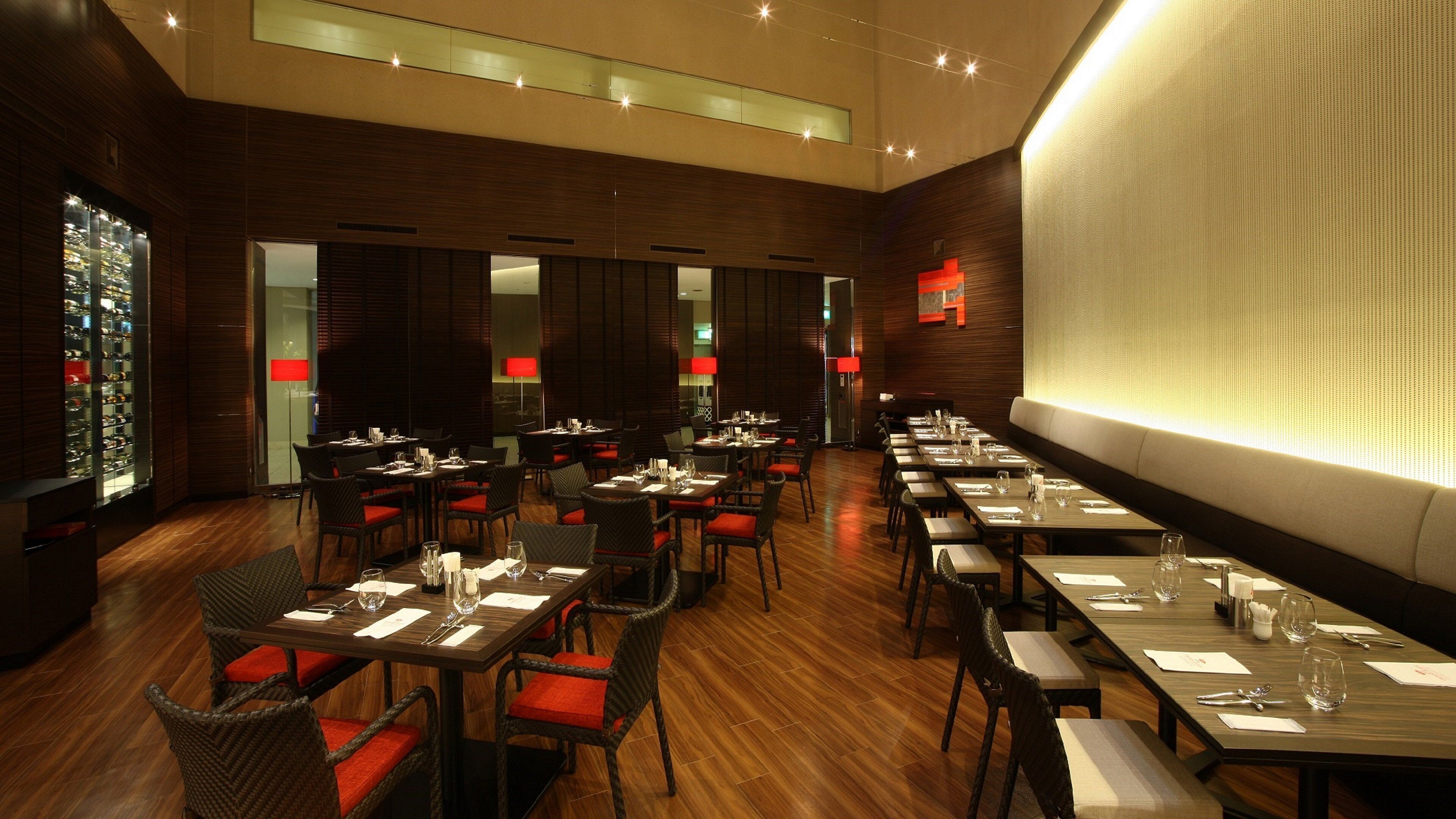 Un restaurante con varias mesas y sillas, una alacena para vinos y una gran pared iluminada.