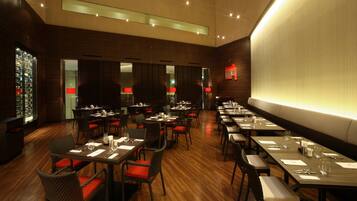 Un restaurante con varias mesas y sillas, una alacena para vinos y una gran pared iluminada.