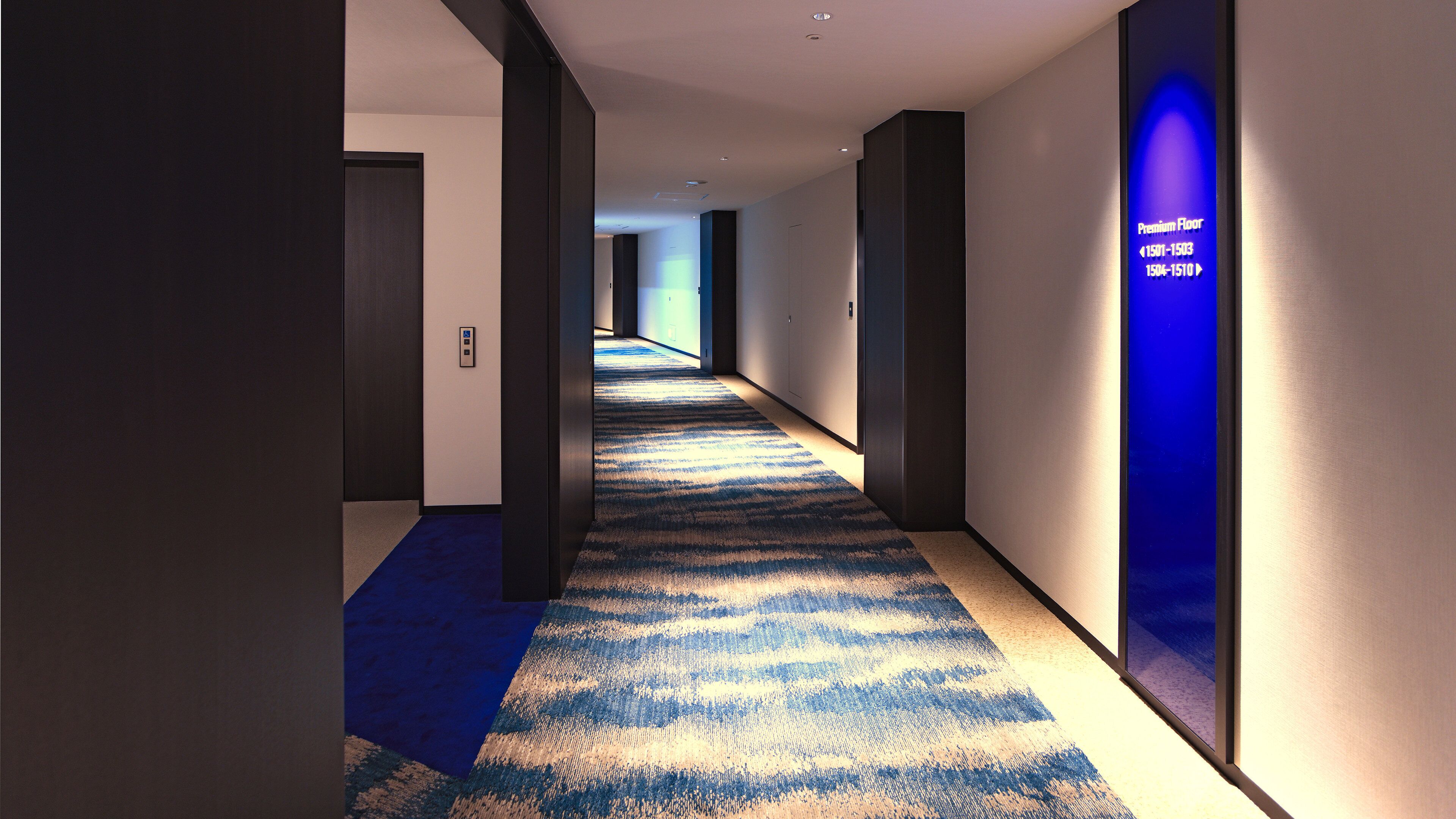 Un pasillo moderno de hotel con alfombra azul, paredes oscuras y un letrero iluminado en azul que indica los pisos premium.