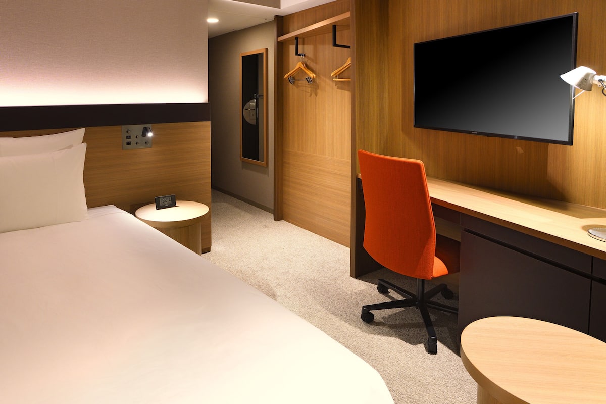 Ein Hotelzimmer mit einem Bett, einem Schreibtisch, einem Stuhl, einem Fernseher und einem Spiegel.