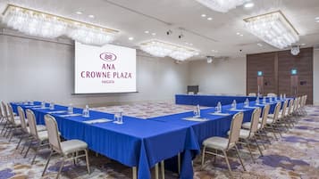 Un salón de conferencias con una pantalla grande mostrando 'ANA CROWNE PLAZA NIIGATA', una mesa larga con sillas y un suelo alfombrado.