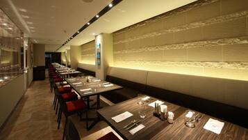 A restaurant with long tables, red cushioned chairs, and a patterned wall.