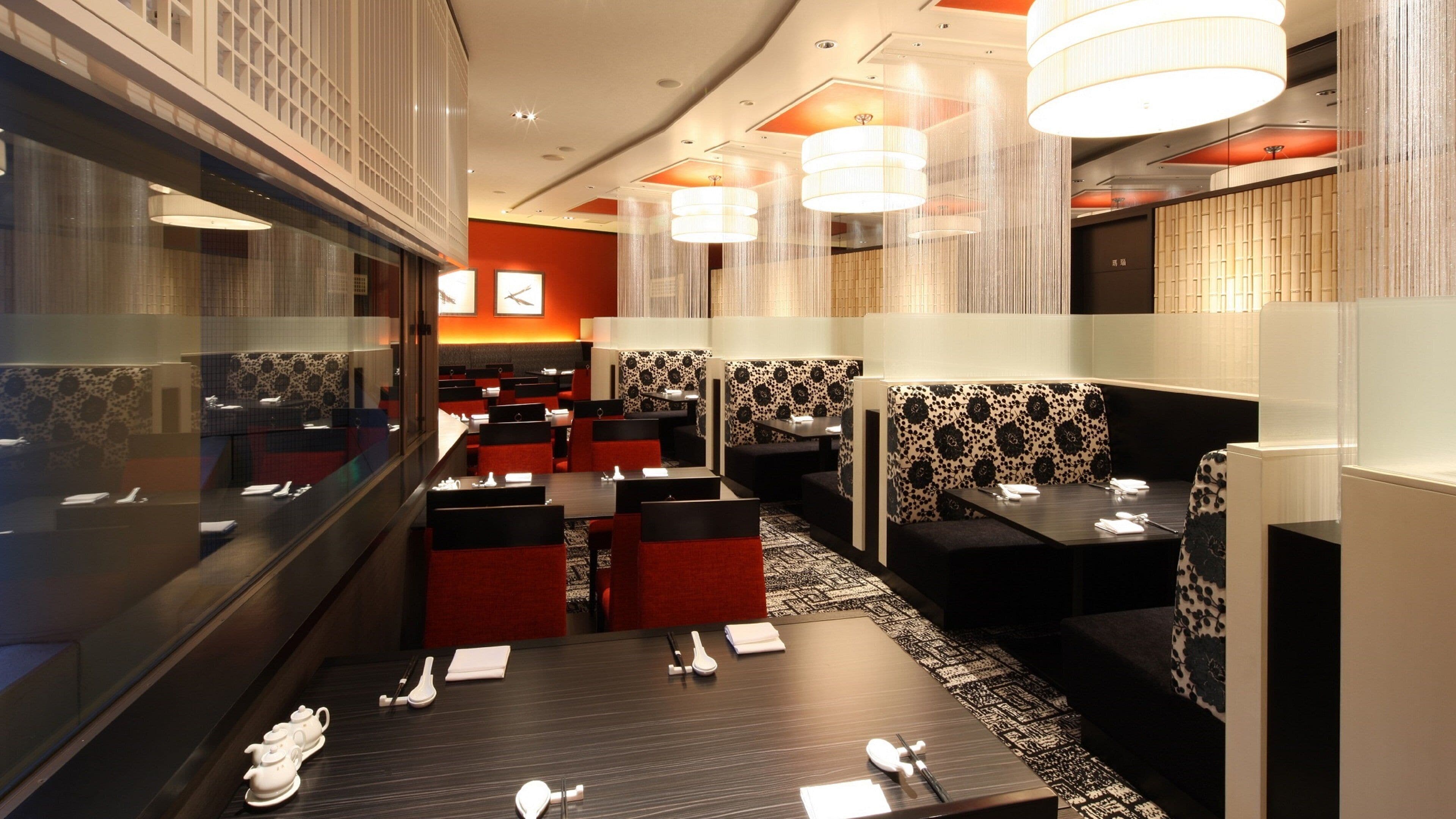 A restaurant with booths and tables, some with red cushions, and a patterned wall.