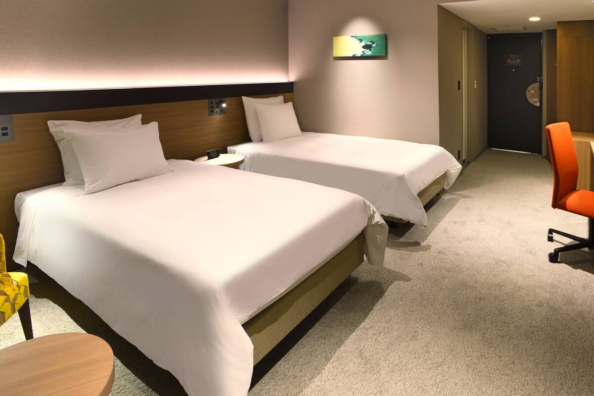 Ein Hotelzimmer mit zwei Betten, einem Schreibtisch, einem Stuhl und einem Fernseher.