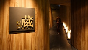 Ein Schild mit japanischen Schriftzeichen und dem Schriftzug 'KU RARA' an einer Wand.
