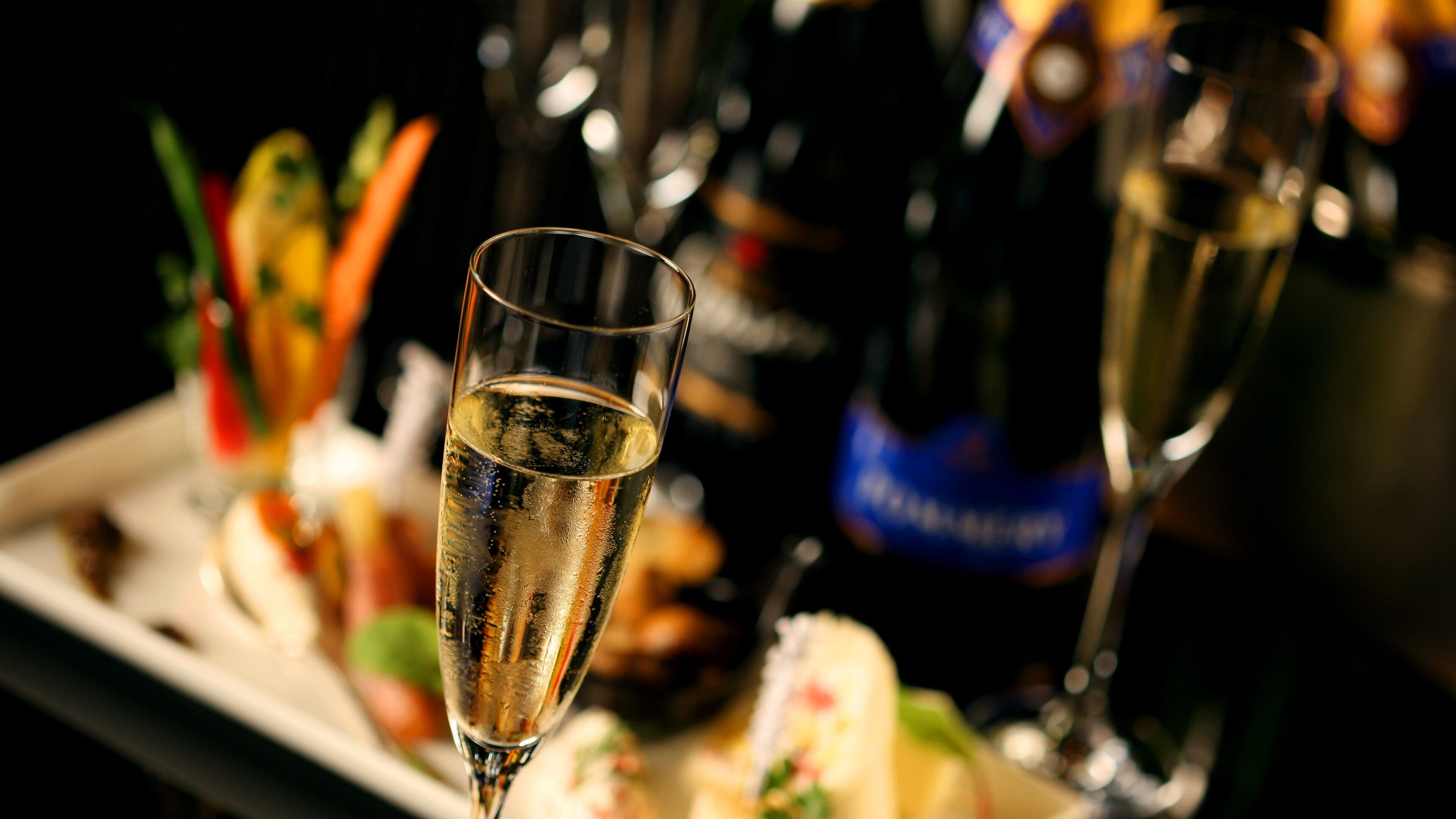 Un verre de champagne sur fond flou de bouteilles et de plats.