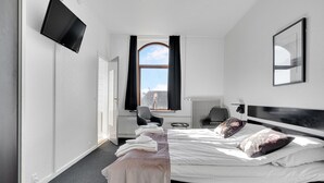 Een moderne hotelkamer met een groot bed, een flatscreen televisie aan de muur, een raam met gordijnen, een radiator en een stoel.