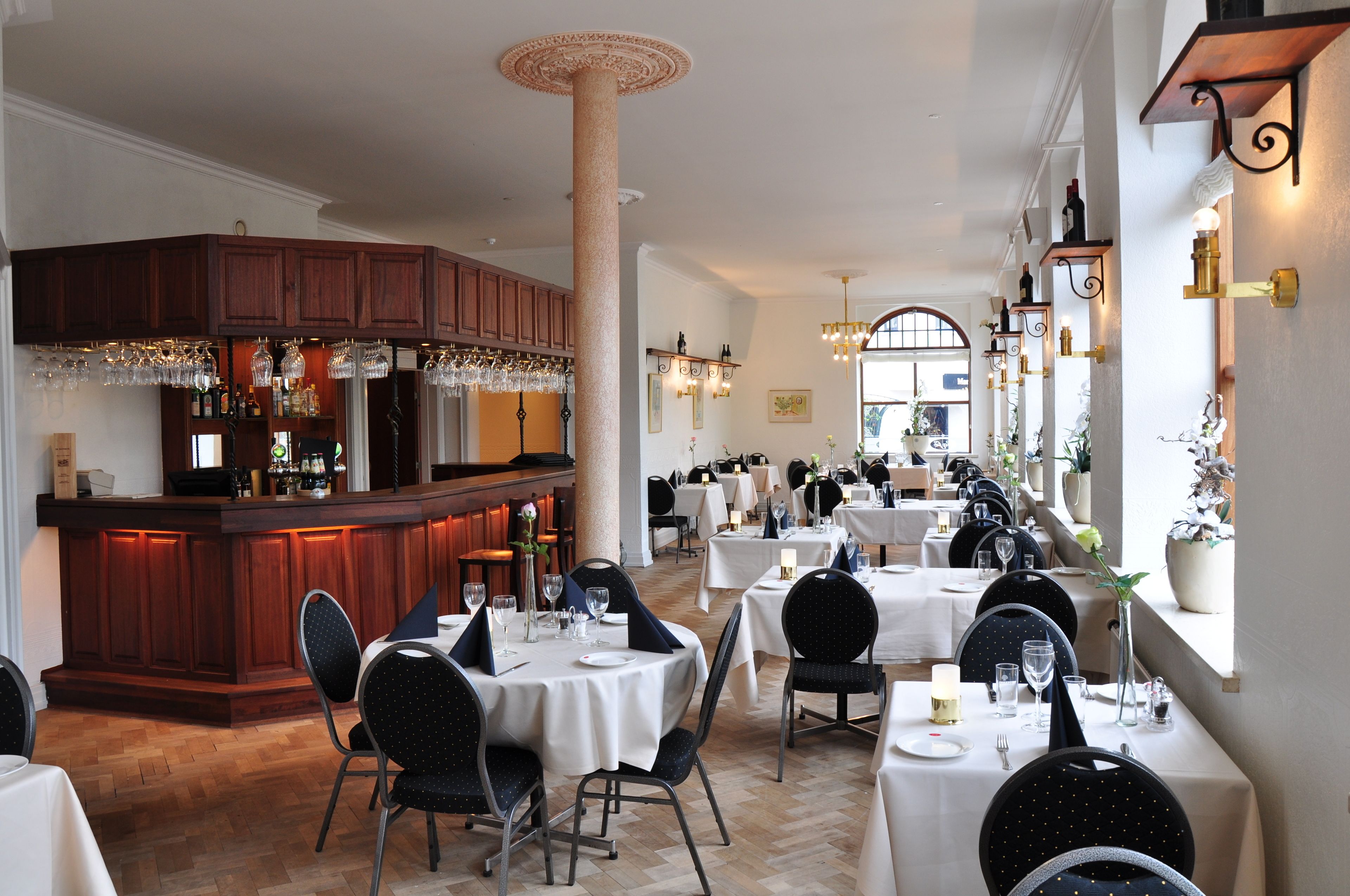 A restaurant with a bar area, multiple tables set for dining, and a column in the center.
