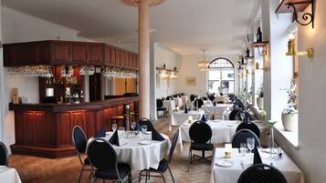 A restaurant with a bar area, multiple tables set for dining, and a column in the center.