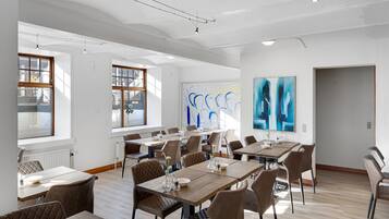 A spacious dining area with multiple tables and chairs, large windows, and abstract art on the walls.