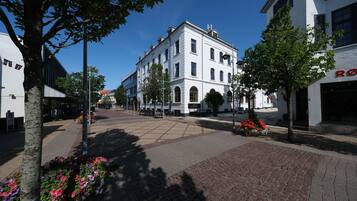 A street with a white building, trees, and flower beds.