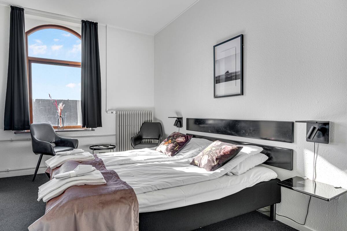 Een moderne hotelkamer met een groot bed, een stoel, een bureau en een raam met gordijnen.