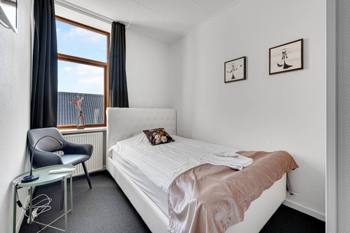Een slaapkamer met een bed, een stoel, een bureau en twee ingelijste foto's aan de muur.