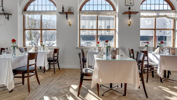 Een eetruimte met tafels gedekt voor vier personen, grote gewelfde ramen en houten vloeren.