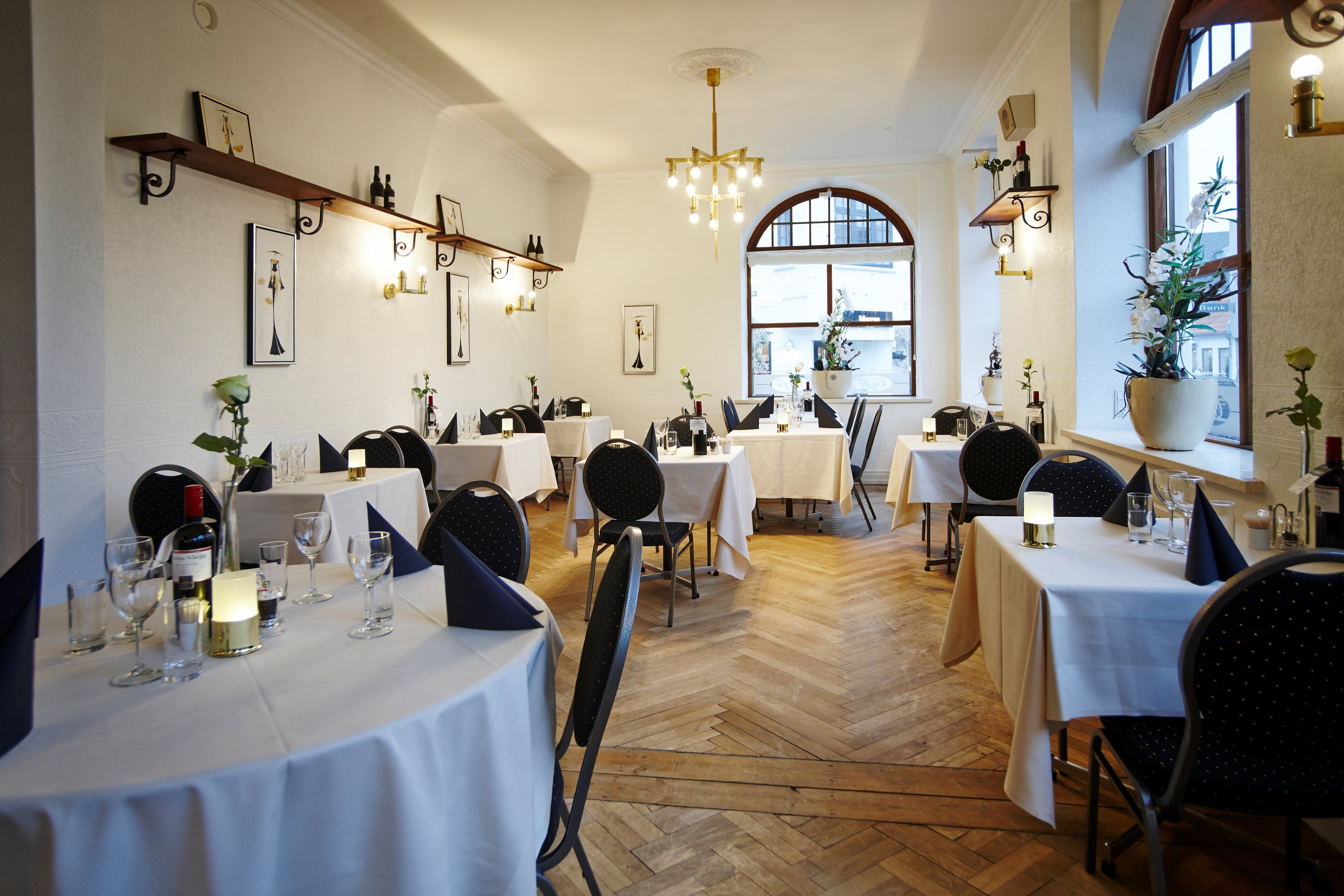 Un restaurante con varias mesas, sillas y un suelo de madera en espiga.